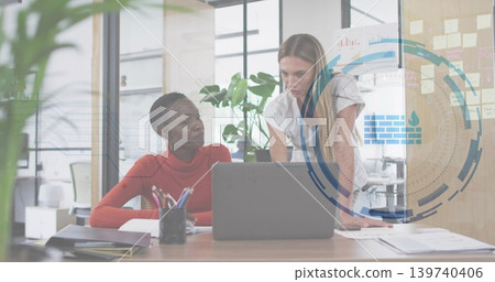 Collaborating women in red top and white blouse reviewing laptop and papers at office with HUD Collaborating women in red top and white blouse reviewing laptop and papers at office with HUD 139740406