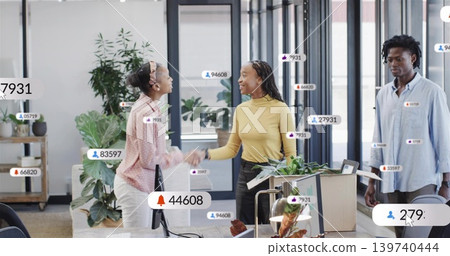 Shaking hands two women wearing business-casual meeting at open-plan office with digital badges Shaking hands two women wearing business-casual meeting at open-plan office with digital badges 139740444