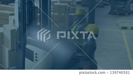Operating forklift, man and woman wearing hard hats checking inventory with clipboard in warehouse Operating forklift, man and woman wearing hard hats checking inventory with clipboard in warehouse 139740581