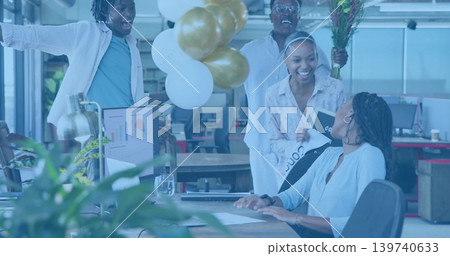 Presenting team celebrating seated coworker in casual business attire at office with balloons Presenting team celebrating seated coworker in casual business attire at office with balloons 139740633
