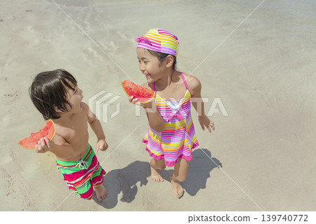 夏天,一對兄妹在海灘邊散步,吃著西瓜。 夏天,一對兄妹在海灘邊散步,吃著西瓜。 139740772