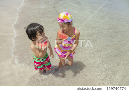 A sister and brother walking along the beach in summer, eating watermelon. A sister and brother walking along the beach in summer, eating watermelon. 139740774
