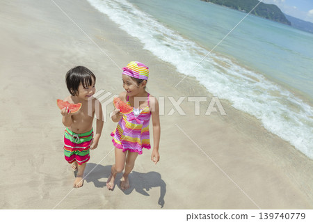 夏天,一對兄妹在海灘邊散步,吃著西瓜。 夏天,一對兄妹在海灘邊散步,吃著西瓜。 139740779