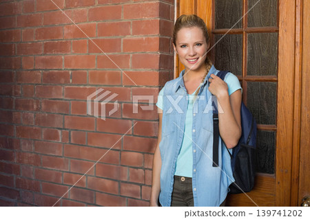 Woman standing at building entrance against red brick wall holding dark backpack strap, copy space 139741202