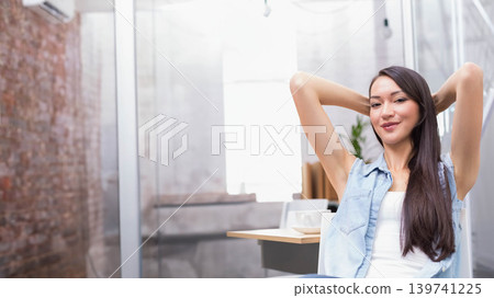 Asian woman sitting at desk in modern office stretching arms with coffee cup, copy space Asian woman sitting at desk in modern office stretching arms with coffee cup, copy space 139741225