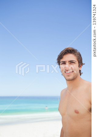 Adult man standing shirtless on sandy beach smiling toward camera with turquoise ocean, copy space 139741324