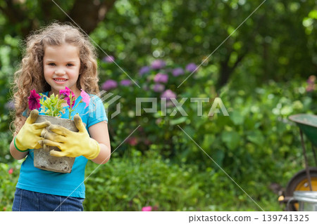 Child girl holding planter with flowers in backyard wearing yellow gloves, denim skirt, copy space 139741325