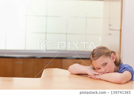 School-age girl leaning with head on arms at kitchen counter, wearing blue top, copy space School-age girl leaning with head on arms at kitchen counter, wearing blue top, copy space 139741365