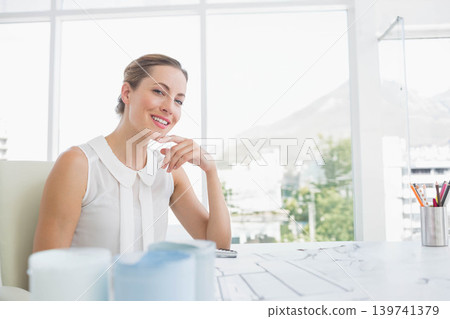 Woman wearing white blouse smiling and posing at desk with building plans, smartphone, copy space 139741379