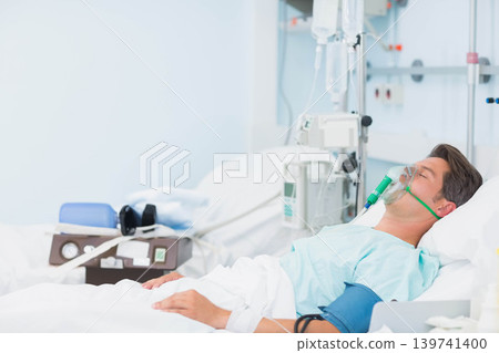 Male patient lying supine on hospital bed receiving oxygen mask and IV pump, copy space 139741400