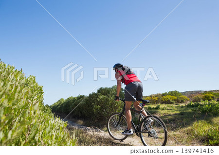 Mature adult man riding mountain bike on sandy trail wearing red top, helmet, pack, copy space Mature adult man riding mountain bike on sandy trail wearing red top, helmet, pack, copy space 139741416