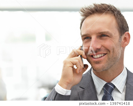 Mid adult man in gray suit holding smartphone to right ear, smiling in office, copy space Mid adult man in gray suit holding smartphone to right ear, smiling in office, copy space 139741418