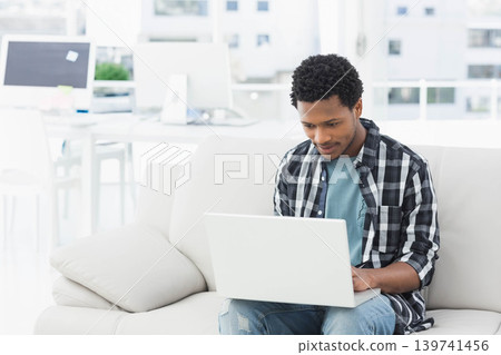 African American man typing on white laptop on beige sofa in bright workspace, copy space 139741456