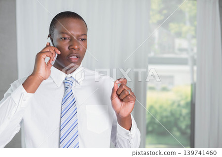 African American man talking on phone, gesturing in white shirt and blue-striped tie at home office African American man talking on phone, gesturing in white shirt and blue-striped tie at home office 139741460