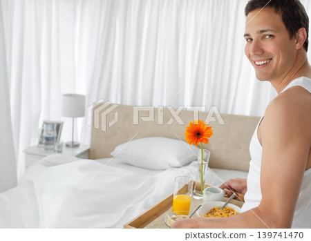 Mid adult man holding wooden tray with gerbera, sitting bed edge wearing tank top, copy space Mid adult man holding wooden tray with gerbera, sitting bed edge wearing tank top, copy space 139741470