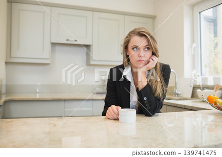 20s woman sitting at kitchen island holding white mug near fruit bowl in blazer, copy space 139741475
