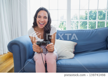 Female sitting on blue sofa in living room in white top pink pants holding wired controller Female sitting on blue sofa in living room in white top pink pants holding wired controller 139741498