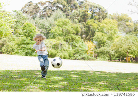 Boy child kicking black-white soccer ball on grassy park lawn wearing white T-shirt jeans and shoes Boy child kicking black-white soccer ball on grassy park lawn wearing white T-shirt jeans and shoes 139741590
