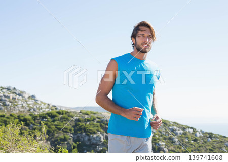 Man in mid twenties running along rocky coastal hillside trail wearing bright blue sleeveless top Man in mid twenties running along rocky coastal hillside trail wearing bright blue sleeveless top 139741608