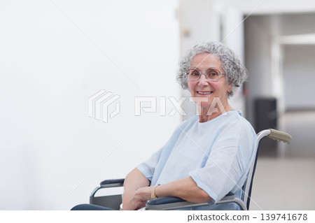 Senior female patient sitting in wheelchair smiling while wearing blue gown in clinic, copy space Senior female patient sitting in wheelchair smiling while wearing blue gown in clinic, copy space 139741678