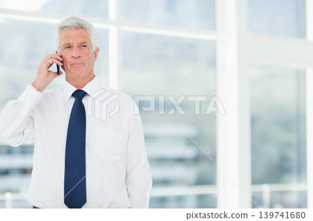 Senior male standing in office by windows holding phone wearing white shirt navy tie, copy space Senior male standing in office by windows holding phone wearing white shirt navy tie, copy space 139741680