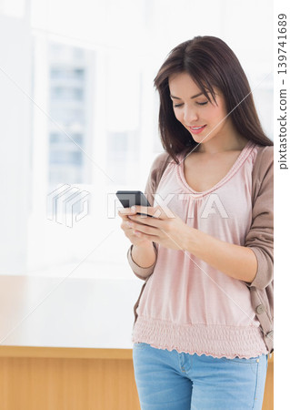 Woman wearing pink blouse checking smartphone by big windows near wooden counter, copy space Woman wearing pink blouse checking smartphone by big windows near wooden counter, copy space 139741689