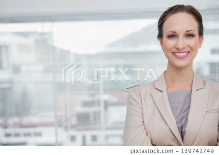Woman in beige blazer smiling and looking toward camera at office by glass window, copy space 139741749