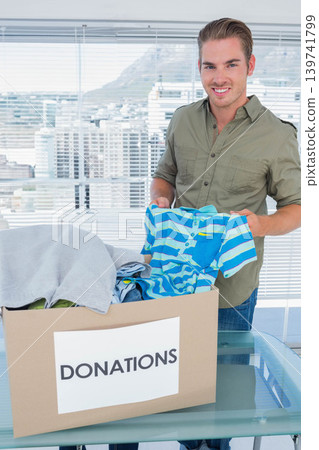 Man standing behind glass table holding child striped shirt sorting into donation box at big window Man standing behind glass table holding child striped shirt sorting into donation box at big window 139741799