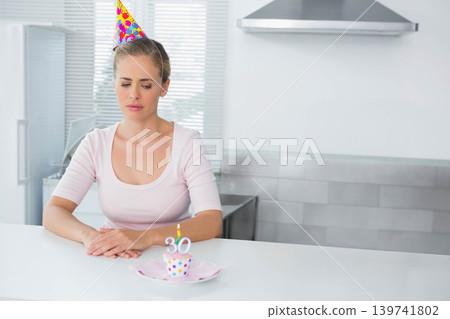 Middle-aged woman wearing party hat, sitting at kitchen counter, looking at cupcake with lit 30 Middle-aged woman wearing party hat, sitting at kitchen counter, looking at cupcake with lit 30 139741802