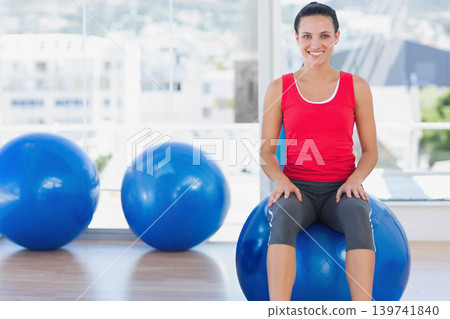 Female sitting on blue exercise ball smiling in studio with large windows, copy space Female sitting on blue exercise ball smiling in studio with large windows, copy space 139741840