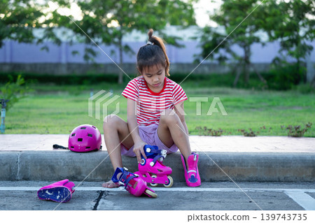 Little girl wearing a pink safety helmet crying and holding her injured elbow after falling down while roller skating. Little girl wearing a pink safety helmet crying and holding her injured elbow after falling down while roller skating. 139743735