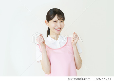 A portrait of a young Japanese female caregiver wearing a pink apron against a white background. A portrait of a young Japanese female caregiver wearing a pink apron against a white background. 139743754