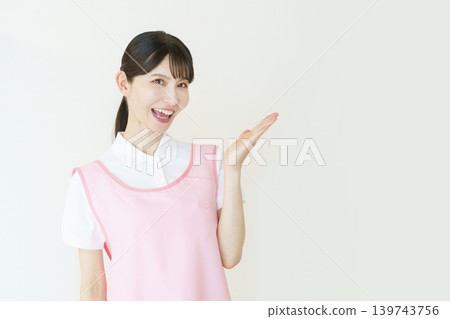 A portrait of a young Japanese female caregiver wearing a pink apron against a white background. A portrait of a young Japanese female caregiver wearing a pink apron against a white background. 139743756
