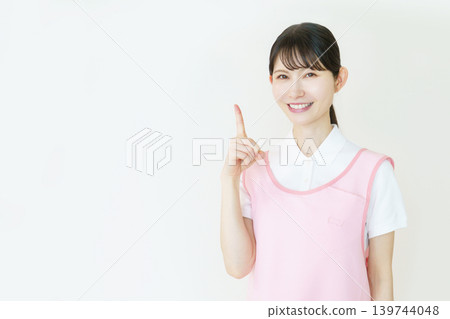 A portrait of a young Japanese female caregiver wearing a pink apron against a white background. A portrait of a young Japanese female caregiver wearing a pink apron against a white background. 139744048
