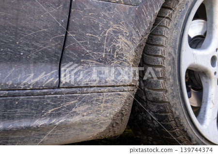 A car is stuck in mud with dirt coating its lower body and mud on the tire. The ground is soft and wet from rain 139744374