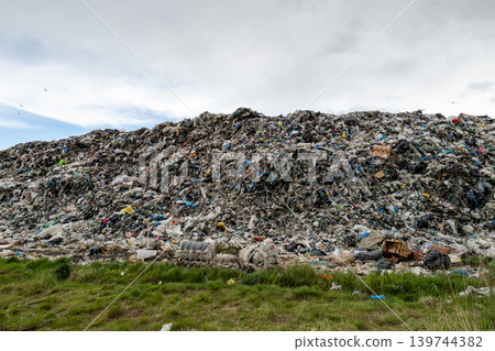 A large pile of waste is seen in a dump site with various types of trash scattered. Birds fly above the garbage in the distance A large pile of waste is seen in a dump site with various types of trash scattered. Birds fly above the garbage in the distance 139744382