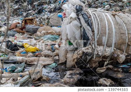 Garbage is stacked in a bale at a waste site with various types of trash scattered around. The scene shows poor waste management practices Garbage is stacked in a bale at a waste site with various types of trash scattered around. The scene shows poor waste management practices 139744383