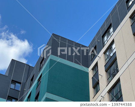 Bright sunlight shines on modern apartment buildings with a clear sky overhead. Blue and gray structures stand tall in the city Bright sunlight shines on modern apartment buildings with a clear sky overhead. Blue and gray structures stand tall in the city 139744388