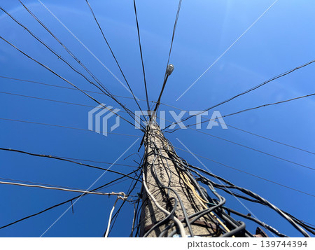 A tall utility pole stands in an open space with many wires extending in different directions under a clear blue sky A tall utility pole stands in an open space with many wires extending in different directions under a clear blue sky 139744394