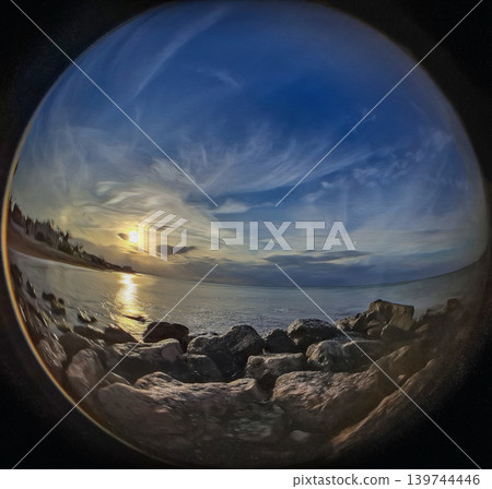 The scene shows a sunset over the coast with a colorful sky. Waves gently crash against the rocks on the beach. The sun sets low in the sky. Clouds gather above, creating a rich atmosphere. The scene shows a sunset over the coast with a colorful sky. Waves gently crash against the rocks on the beach. The sun sets low in the sky. Clouds gather above, creating a rich atmosphere. 139744446