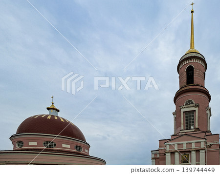 The Orthodox church features a pink exterior, a large dome, and a tall golden spire with a cross. The sky is cloudy, creating a striking backdrop for the structure. The Orthodox church features a pink exterior, a large dome, and a tall golden spire with a cross. The sky is cloudy, creating a striking backdrop for the structure. 139744449