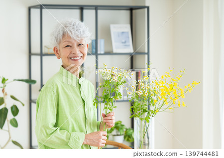A senior woman putting flowers in a vase at home. A senior woman putting flowers in a vase at home. 139744481