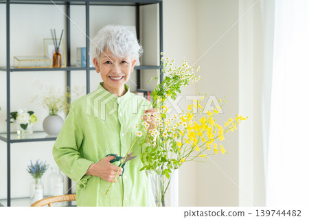 A senior woman putting flowers in a vase at home. A senior woman putting flowers in a vase at home. 139744482