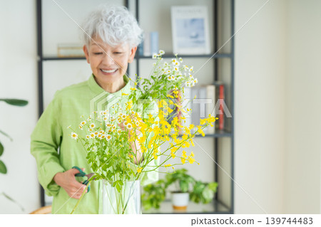 A senior woman putting flowers in a vase at home. 139744483