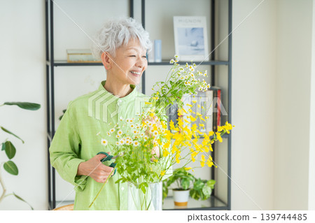 A senior woman putting flowers in a vase at home. A senior woman putting flowers in a vase at home. 139744485