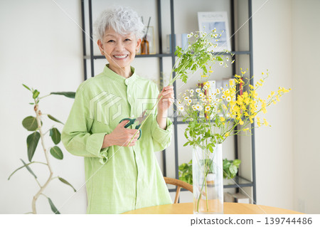 A senior woman putting flowers in a vase at home. 139744486