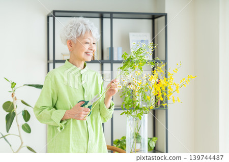 一位老婦人在家裡的花瓶裡插花。 一位老婦人在家裡的花瓶裡插花。 139744487