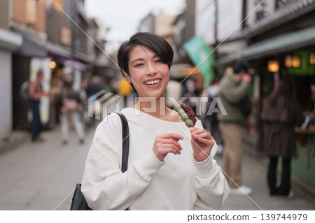 Portrait of a woman enjoying sightseeing while eating Japanese sweets. Portrait of a woman enjoying sightseeing while eating Japanese sweets. 139744979