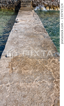 Weathered concrete pier leading to stone stairs by the sea 139745124