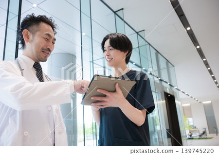 畫面中,醫生一邊看著平板電腦一邊給予指示和傳遞訊息,旁邊還有一位新來的醫生或護士,這體現了醫療領域的數位轉型(DX)和團隊合作。 畫面中,醫生一邊看著平板電腦一邊給予指示和傳遞訊息,旁邊還有一位新來的醫生或護士,這體現了醫療領域的數位轉型(DX)和團隊合作。 139745220